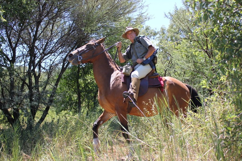 Les Brett on horseback moving through thick bush on an anti-poaching patrol.