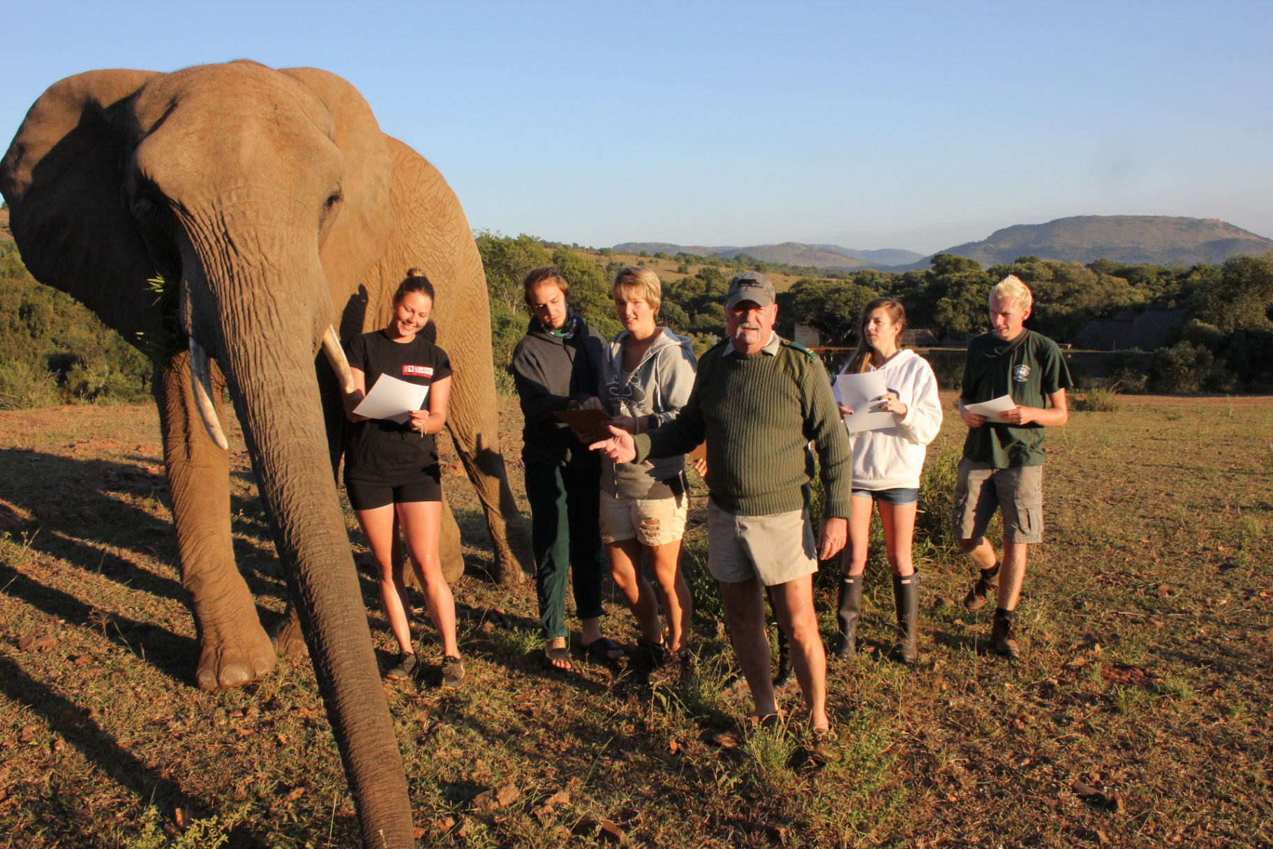 Les Brett teaching students in the field beside a young elephant.
